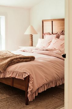 a bed with pink sheets and pillows in a bedroom next to a lamp on a table