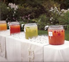 four jars filled with liquid sitting on top of a table covered in white cloths