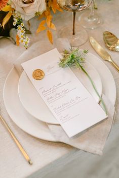 a table set with white plates and silverware, gold utensils and floral centerpieces