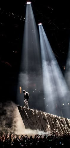 a man standing on top of a large rock under three spotlights in the dark