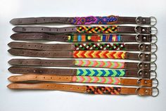 several different colored belts are lined up on a white surface, one is brown and the other has multicolored braiding