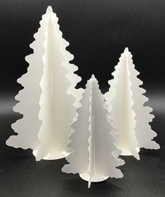 three white paper christmas trees on a black surface