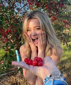 a woman holding two cherries in her hand while standing next to an apple tree