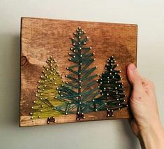 a person holding up a wooden board with string work on it and small pine trees