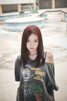 a woman with red hair standing in front of a swimming pool wearing a t - shirt