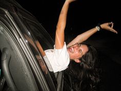 a woman sticking her head out the window of a car at night with her arms in the air