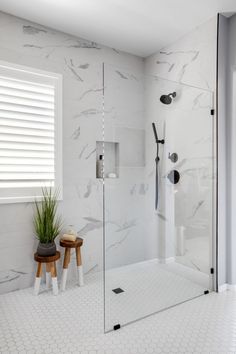 a walk in shower sitting next to a white tiled wall and wooden stool on the floor