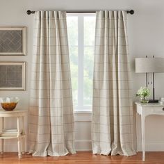 a living room with white walls and wooden flooring, two windows covered in beige plaid curtains