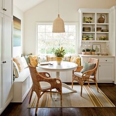 a kitchen with white walls and wooden flooring next to a dining room table surrounded by wicker chairs