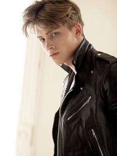 a young man in a black leather jacket looking off to the side with his hand on his hip