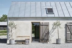 a small white building with two doors and a bench in front of it on gravel ground