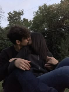 a man and woman sitting on the ground kissing each other with trees in the background