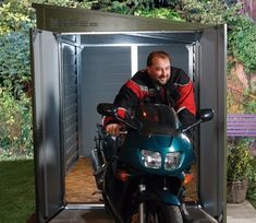 a man sitting on a motorcycle in front of a storage shed with the door open