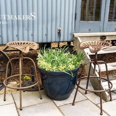 two chairs and a table with plants in them on the side of a train track