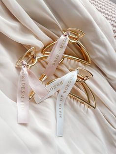 three gold hair clips on top of a white satin material with words written on them