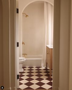 an open door leading to a bathroom with a checkered floor and white tub in the corner