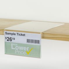 a new lower price ticket sitting on top of a wooden shelf next to a white wall