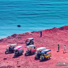 four vehicles parked on the beach with people standing around