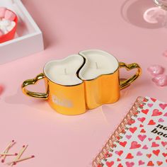 two yellow coffee mugs sitting on top of a pink table