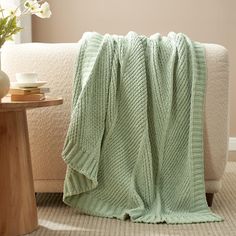 a green blanket sitting on top of a couch next to a vase with white flowers