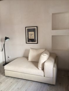 a white couch sitting next to a lamp on top of a hard wood floored floor