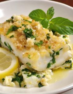 a white plate topped with fish covered in sauce and garnished with green leaves