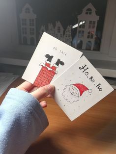 two children's hand holding up christmas cards with santa and chimney on the front