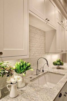 a kitchen with marble counter tops and white cabinets, along with two vases filled with flowers