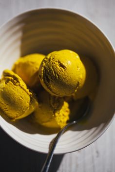 three scoops of yellow ice cream in a white bowl