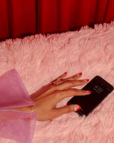 a woman's hand holding a cell phone on top of a fluffy pink blanket