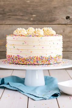 a white cake with sprinkles on it sitting on a table next to a plate