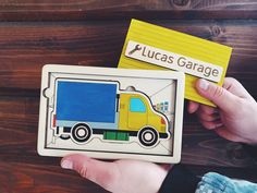 a child's hand holding a wooden puzzle with a truck on it and a name tag that says lucas garage