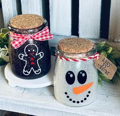 two decorated jars sitting on top of a white table next to each other, one has a gingerbread man and the other has a snowman