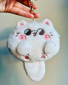 a white cat keychain hanging from a hand