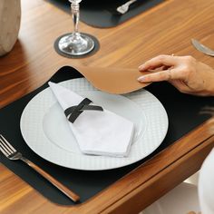 a person is setting a table with white plates and silverware, napkins and utensils