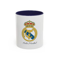 a white and blue coffee mug with the real madrid crest on it's side