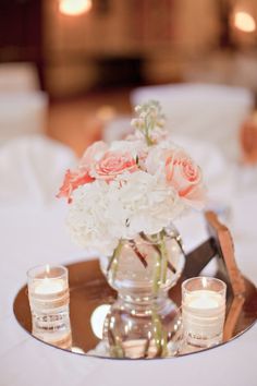 a vase filled with white and pink flowers on top of a metal tray next to candles