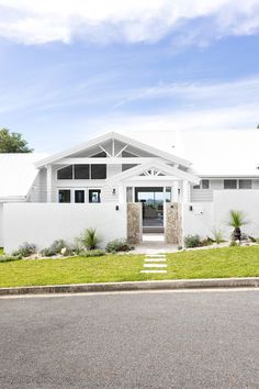 White coastal home exterior with stone feature wall and A-frame pitched roofline. Front Fence Ideas, Coastal House Exterior, Coastal Facade, Serene Interior, Coastal Home Exterior, Modern Coastal Farmhouse, Stone Feature Wall, 80s House, Coastal Exterior