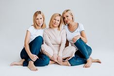 three women are sitting on the floor posing for a photo with their arms around each other