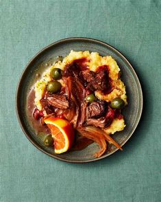 a plate filled with meat and vegetables on top of mashed potatoes next to an orange slice