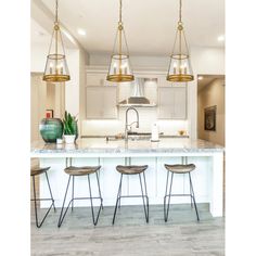 a kitchen island with four stools in front of it and lights hanging from the ceiling