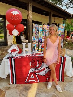 a woman standing in front of a table with balloons on it and a banner behind her