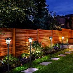 an outdoor garden at night with lights on the fence and grass in the foreground