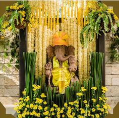 an elephant statue sitting on top of a lush green field next to yellow and white flowers