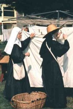 two women dressed in black and white are hanging clothes on a line with a wicker basket next to them