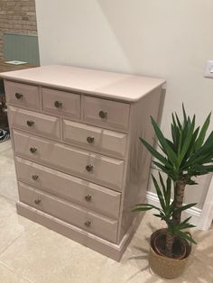 a white dresser next to a potted plant on the floor