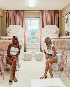 two women sitting on chairs in a room with white furniture and pink curtains, all smiling at the camera