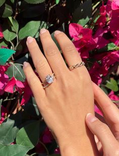 a woman's hand with a diamond ring on it and pink flowers in the background