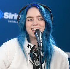 a woman with blue hair is wearing headphones and smiling at the camera while sitting in front of a microphone