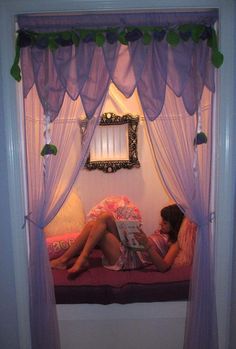 a woman sitting on top of a bed under a purple canopy over it's head